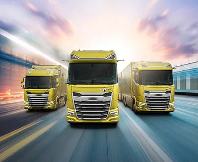 Three yellow Automobile trucks drive side by side on a highway, with motion blur in the background indicating high speed.